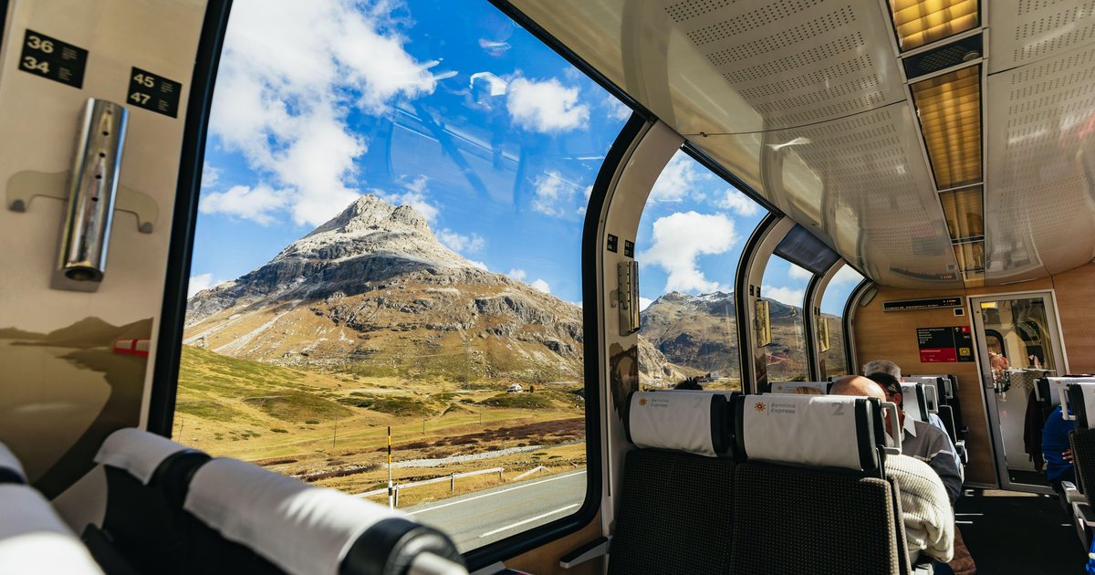 Inside a panoramic car of the Bernina Express, with large windows reaching into the roof and mountains outside