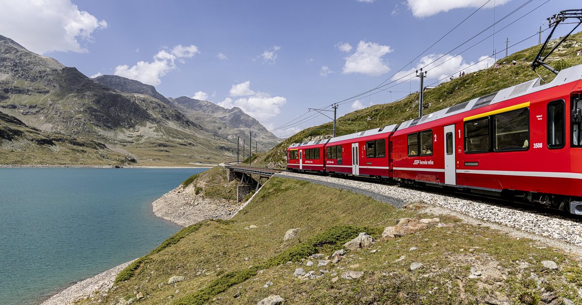 The red Bernina train running along the shore of Lago Bianco near the Bernina Pass, with glaciers behind